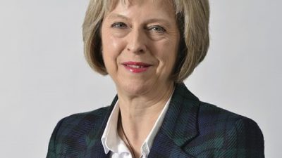 Theresa May i rutig kavaj ler.