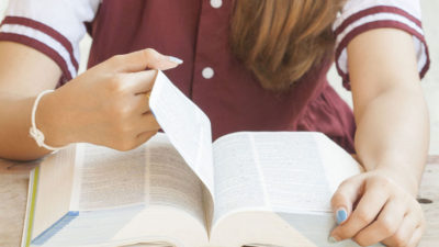 Ett lexikon ligger på ett bord. En person, där ansiktet inte syns, bläddrar i den tjocka boken.