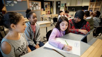 Några tjejer sitter vid en bänk. En av dem skriver ner frågor.