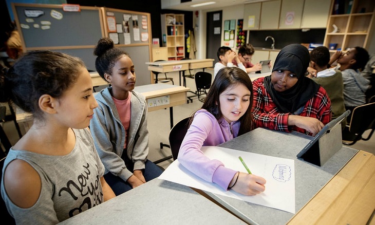 Några tjejer sitter vid en bänk. En av dem skriver ner frågor.