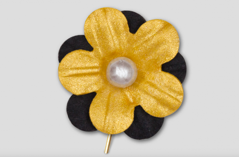 En pappersblomma på en nål. Blomman är guldig med svarta blad runt.
