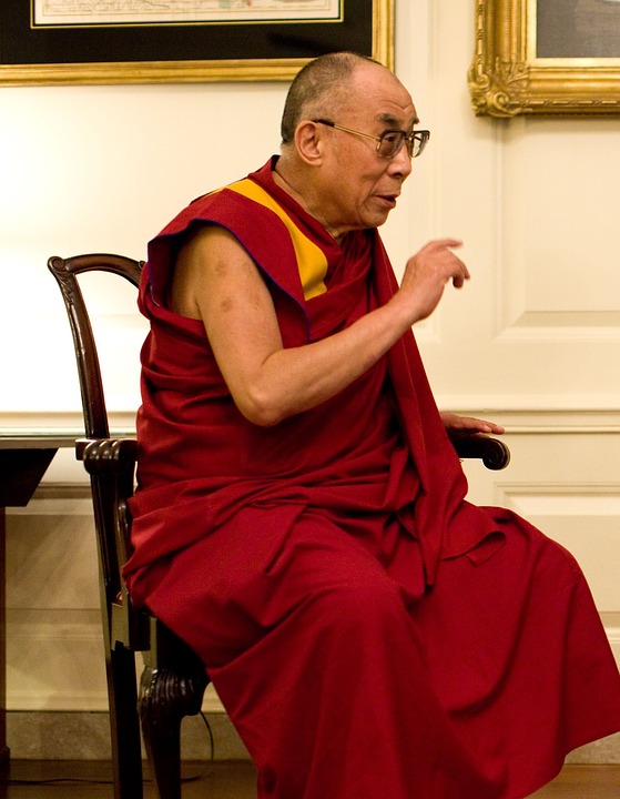 Dalai Lama sitter på en stol i en röd kläsel