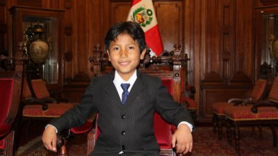 José sitter i en stor trästol. Han har kostym och slips på sig. Han har svart kort hår som är delat i en mittbena och ler mot kameran. I bakgrunden syns Perus flagga.