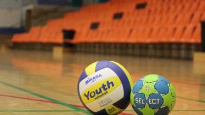 Två handbollar ligger på ett golv i en idrottshall.