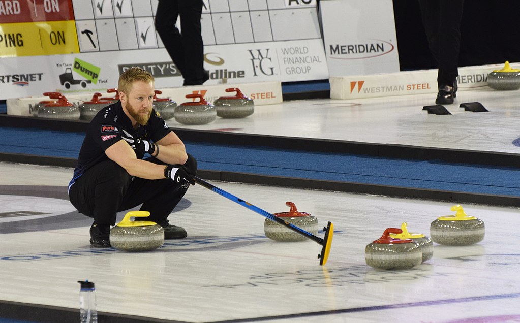 Bild på Niklas Edin under en match. Han står hukad på isen och pekar var hans medspelare ska träffa curlingstenen för att slå bort motståndarna.