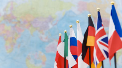 G7-ländernas falggor hänger i rad. Bakom dem syns en världskarta.